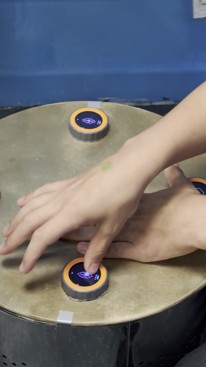 Zwei Hände am TAMBUM-Tisch: ein Finger drückt eine Scheibe, auf deren Display ein Muster steht